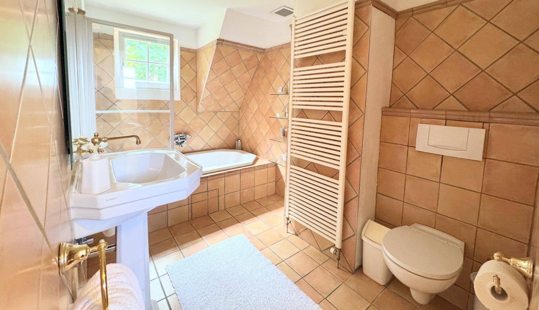 Badezimmer mit Terrakottafliesen, Badewanne, Waschtisch und beheiztem Handtuchhalter.