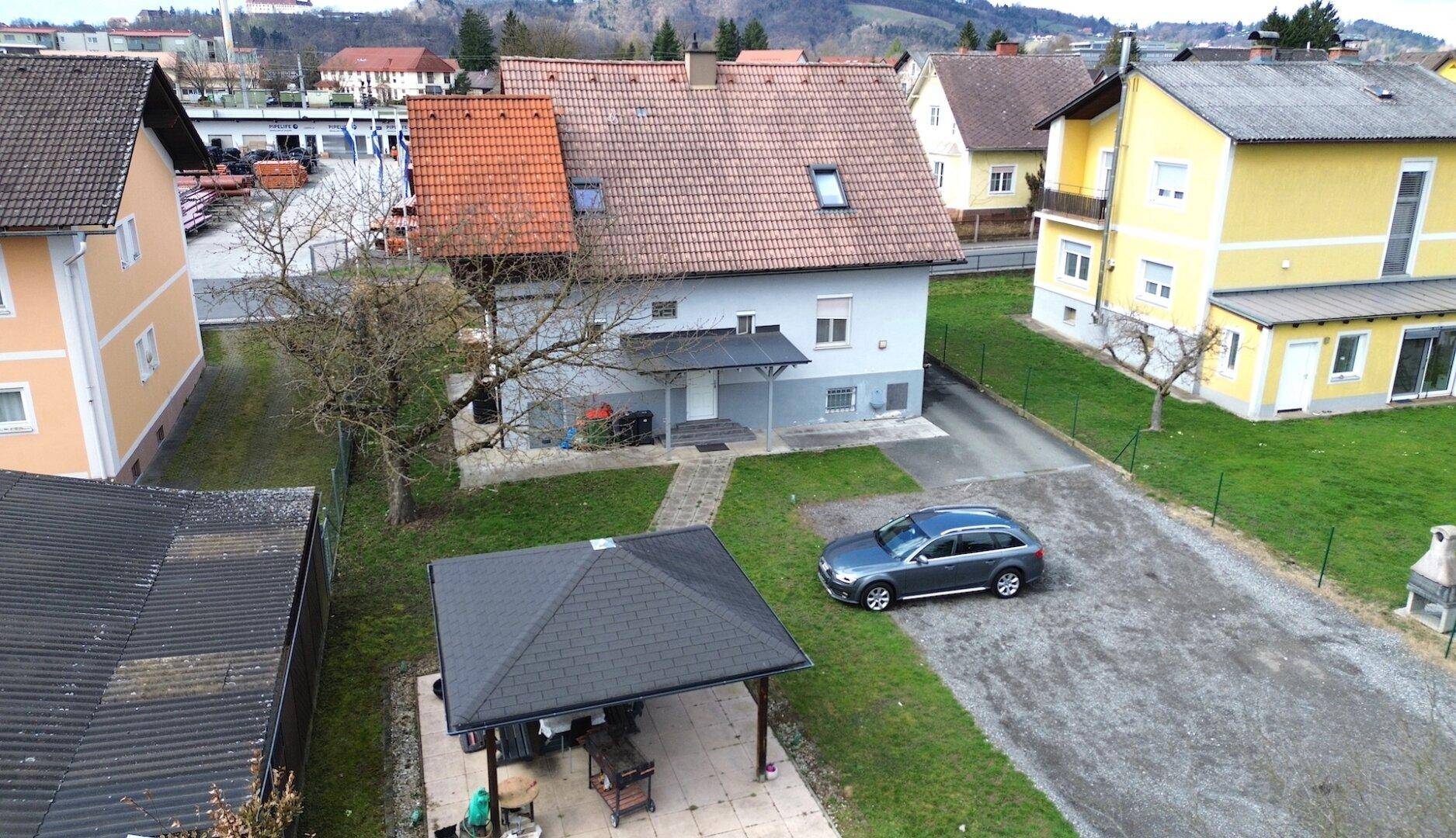 Luftaufnahme des Hauses mit großem Garten, Carport und geparktem Auto auf dem Grundstück.