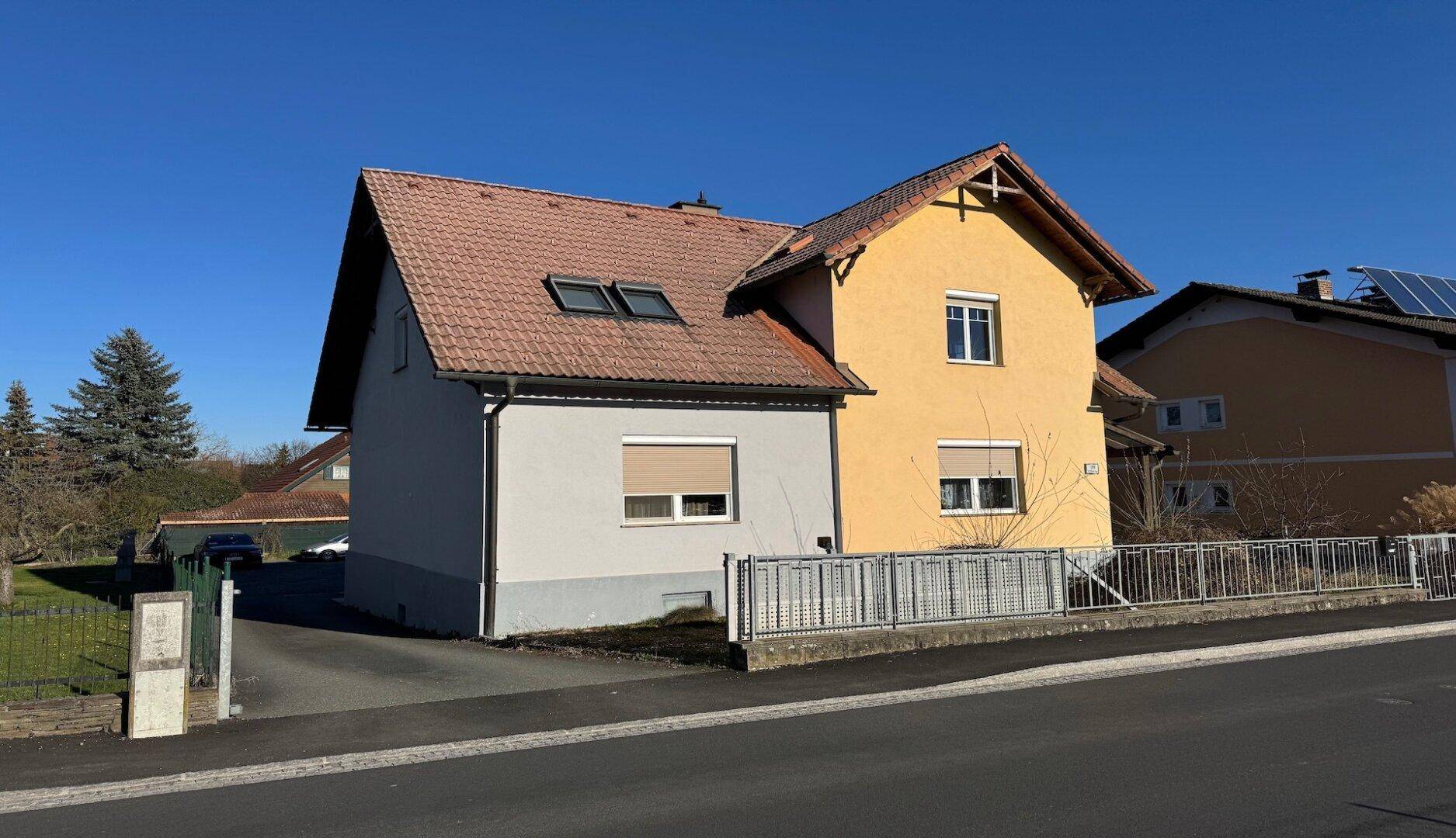Frontansicht des Hauses mit Vorgarten und Zufahrt an einem sonnigen Tag mit blauem Himmel.