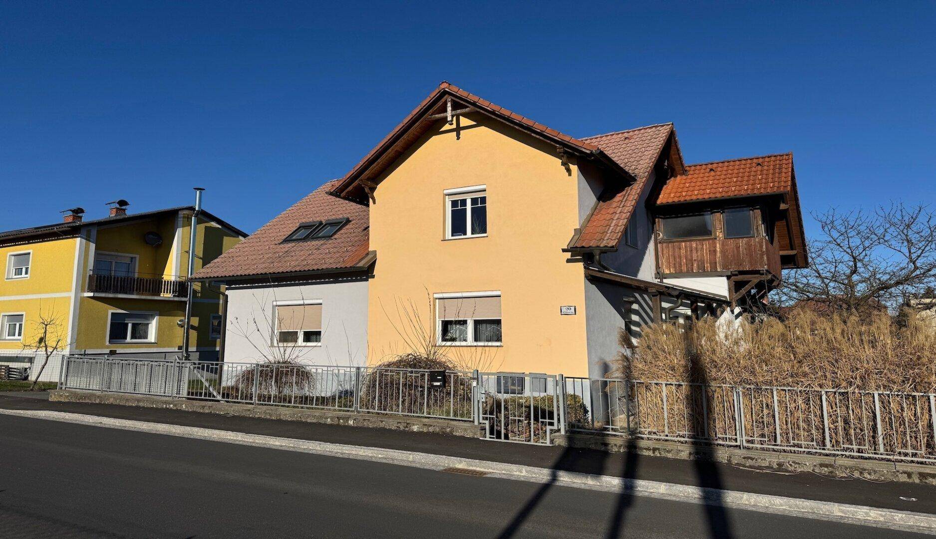 Seitenansicht des Hauses mit Balkon und Vorgarten, umgeben von Hecken und Bäumen.