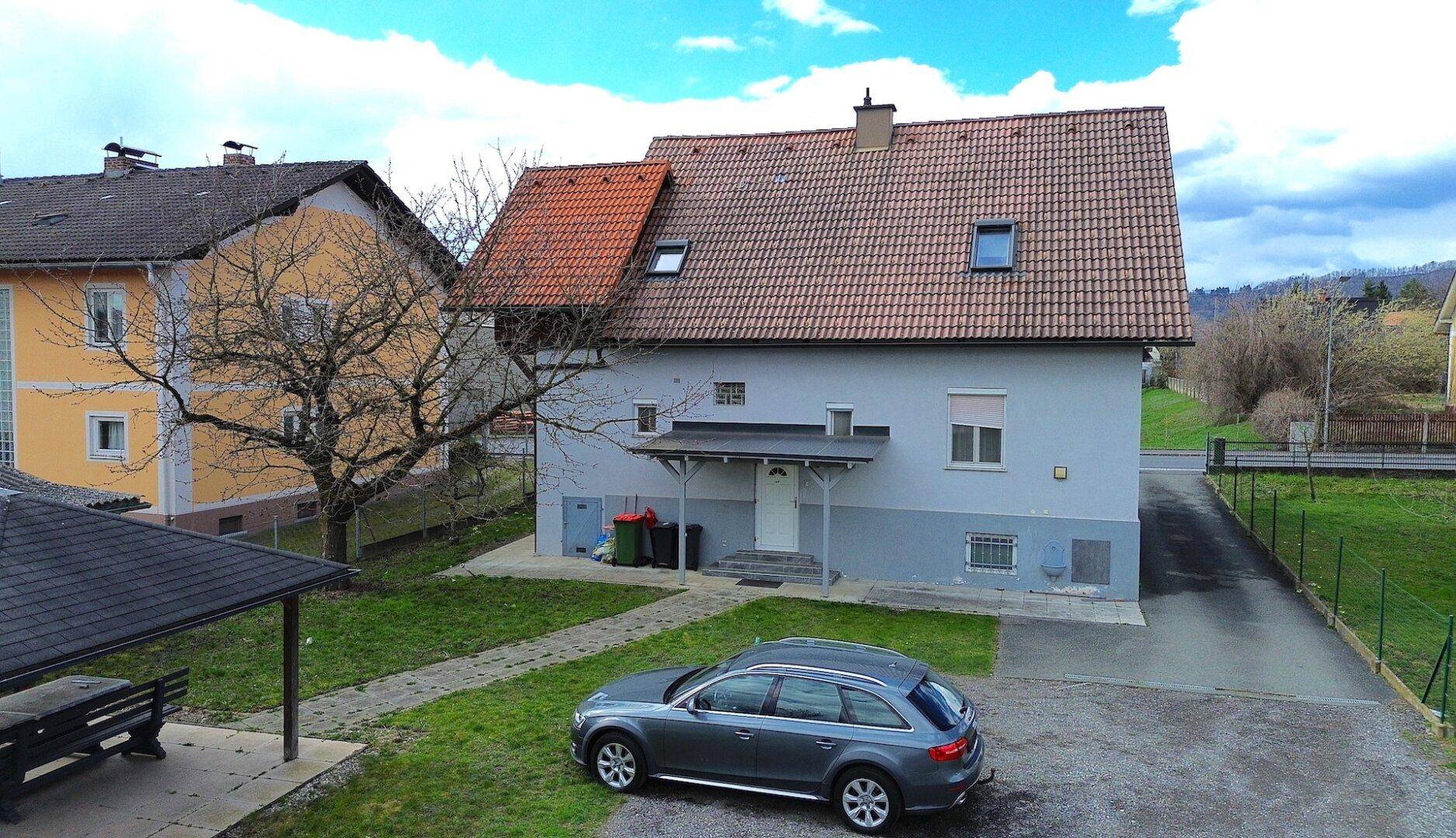 Luftaufnahme des Hauses von hinten mit Garten, Carport und geparktem Auto auf dem Grundstück.