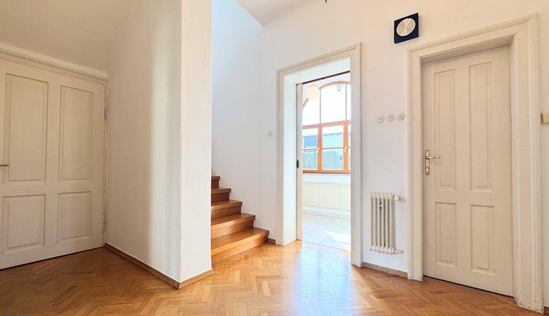 Geräumiger Flur mit Fischgrätparkettboden und Holztreppe, die in die oberen Stockwerke führt.