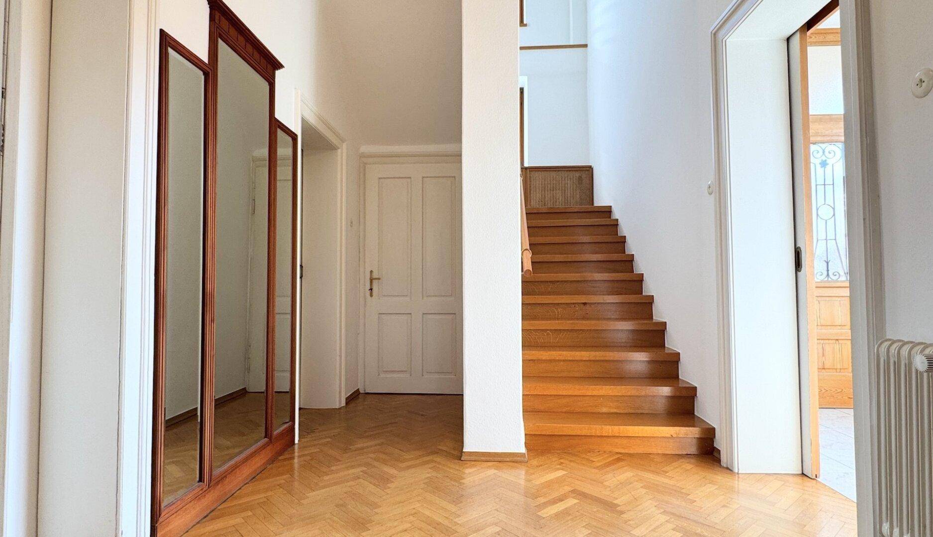 Heller Flur mit Holztreppe, Fischgrätparkett und großen Spiegeln, die den Raum optisch erweitern.