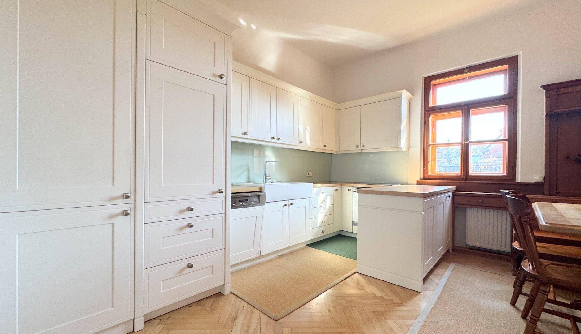 Traditionelle Küche mit weißen Einbauschränken, Holzparkett und einem Fenster, das viel Licht spendet.