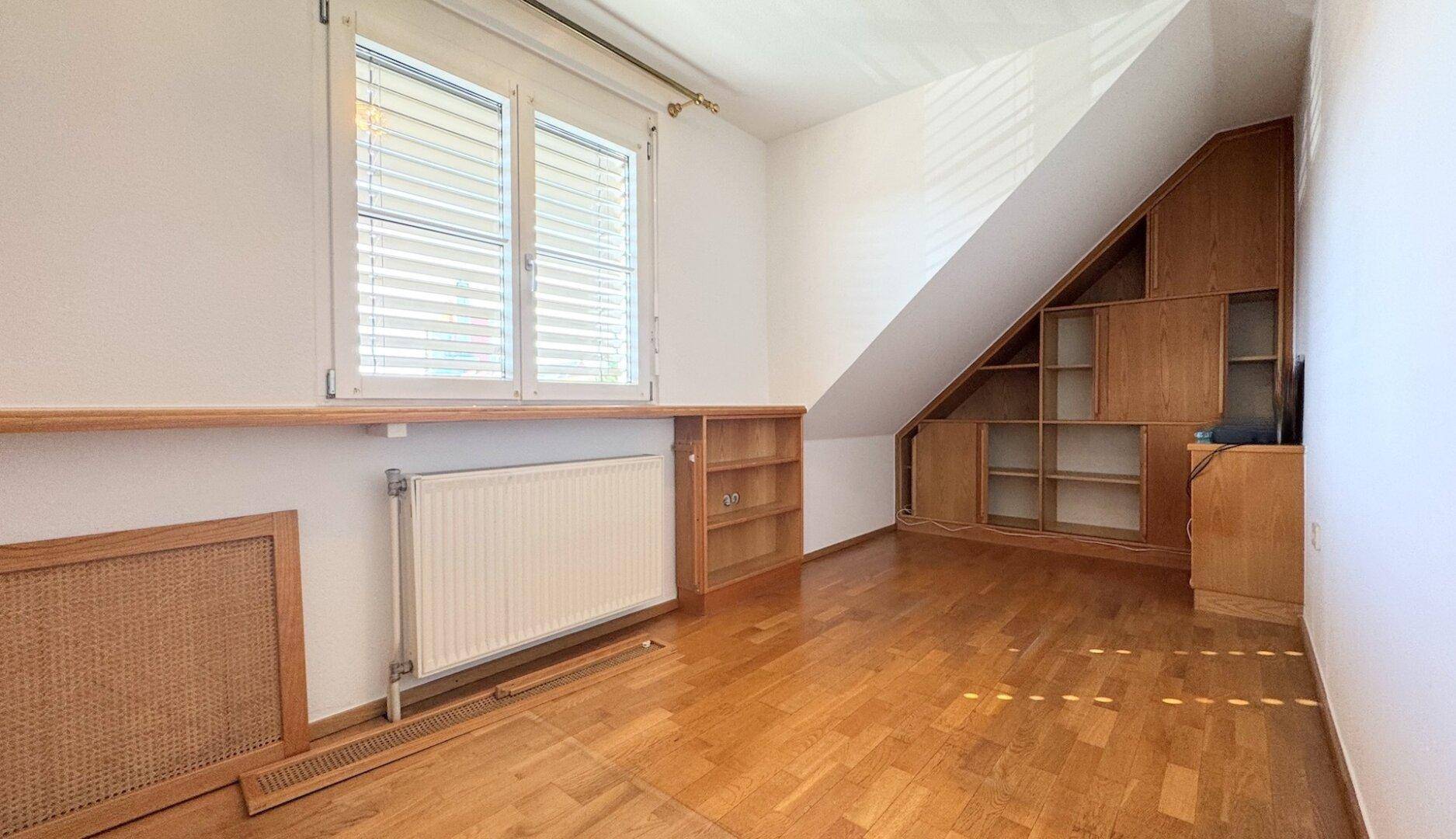 Zimmer mit Holzparkett, Dachschräge und integrierten Holzregalen und Schränken.