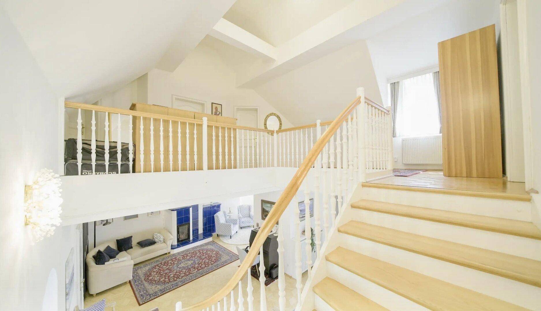 Elegante Holztreppe führt zu einer offenen Galerie mit Blick auf den darunterliegenden Wohnbereich.