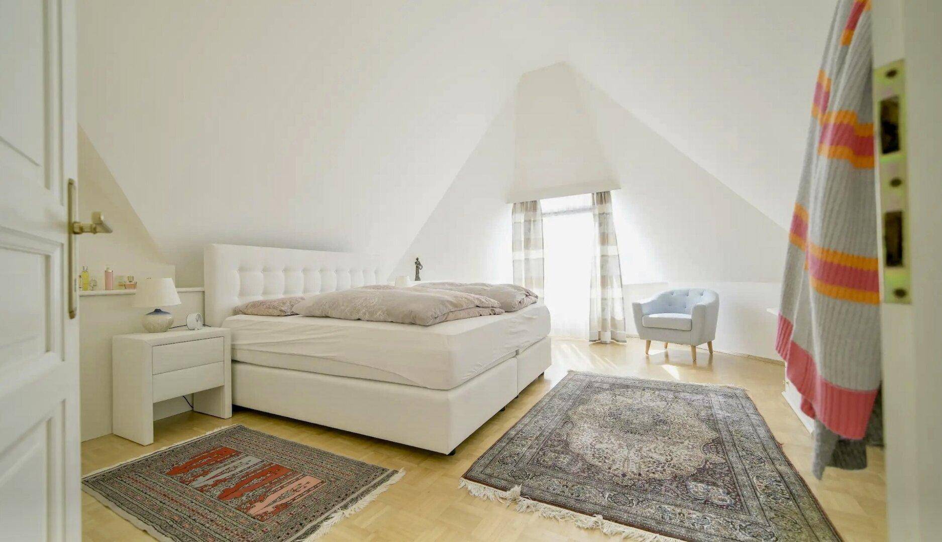 Gemütliches Schlafzimmer im Dachgeschoss mit Dachschrägen, Doppelbett und Teppichen auf Parkettboden.