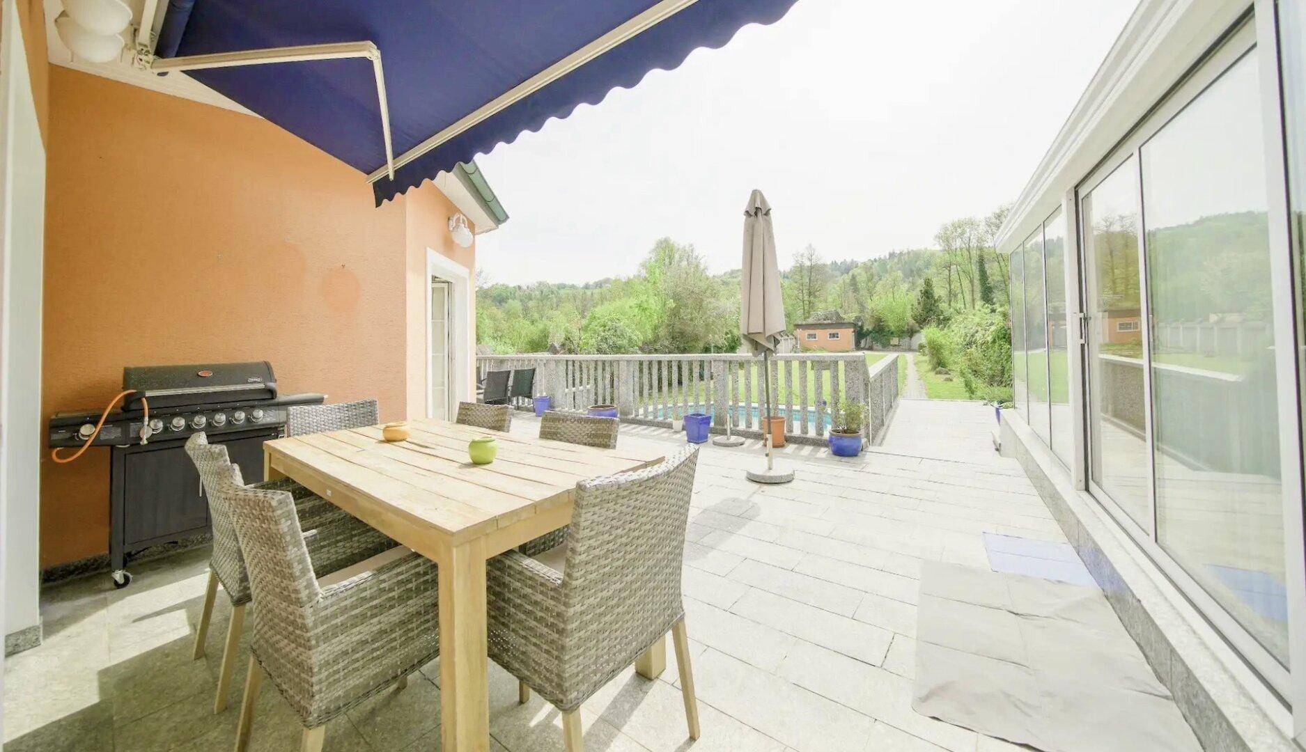 Große Sonnenterrasse mit Esstisch, Grillbereich und Blick ins Grüne, ideal für Mahlzeiten im Freien.