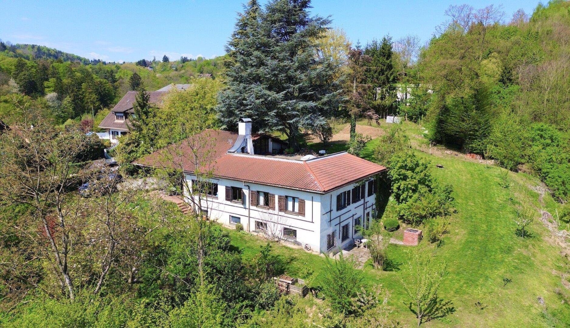 Luftaufnahme des Landhauses mit rotem Ziegeldach, eingebettet in eine grüne Hügellandschaft.