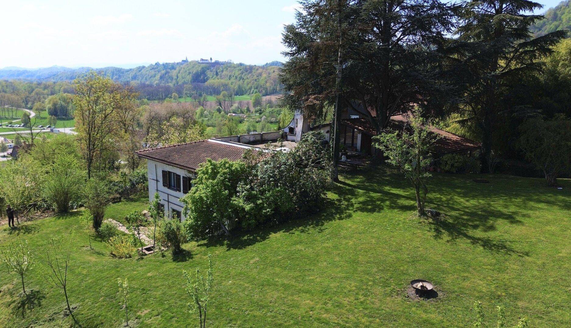 Luftaufnahme des Anwesens mit weitläufigem Rasen und altem Baumbestand in sonniger Lage.