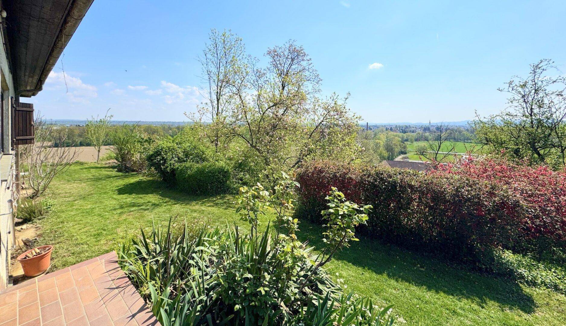 Gepflasterte Terrasse mit Blick auf den gepflegten Garten und die weite Landschaft.