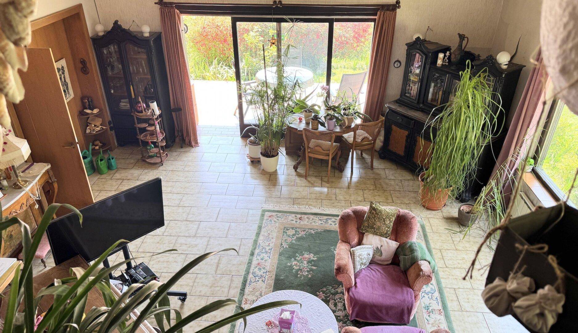Geräumiges Wohnzimmer mit Fliesenboden, vielen Pflanzen und Zugang zur Terrasse.