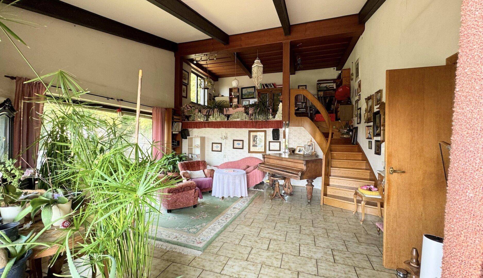 Helles Wohnzimmer mit hoher Decke, sichtbaren Holzbalken und Treppe zur Galerie.