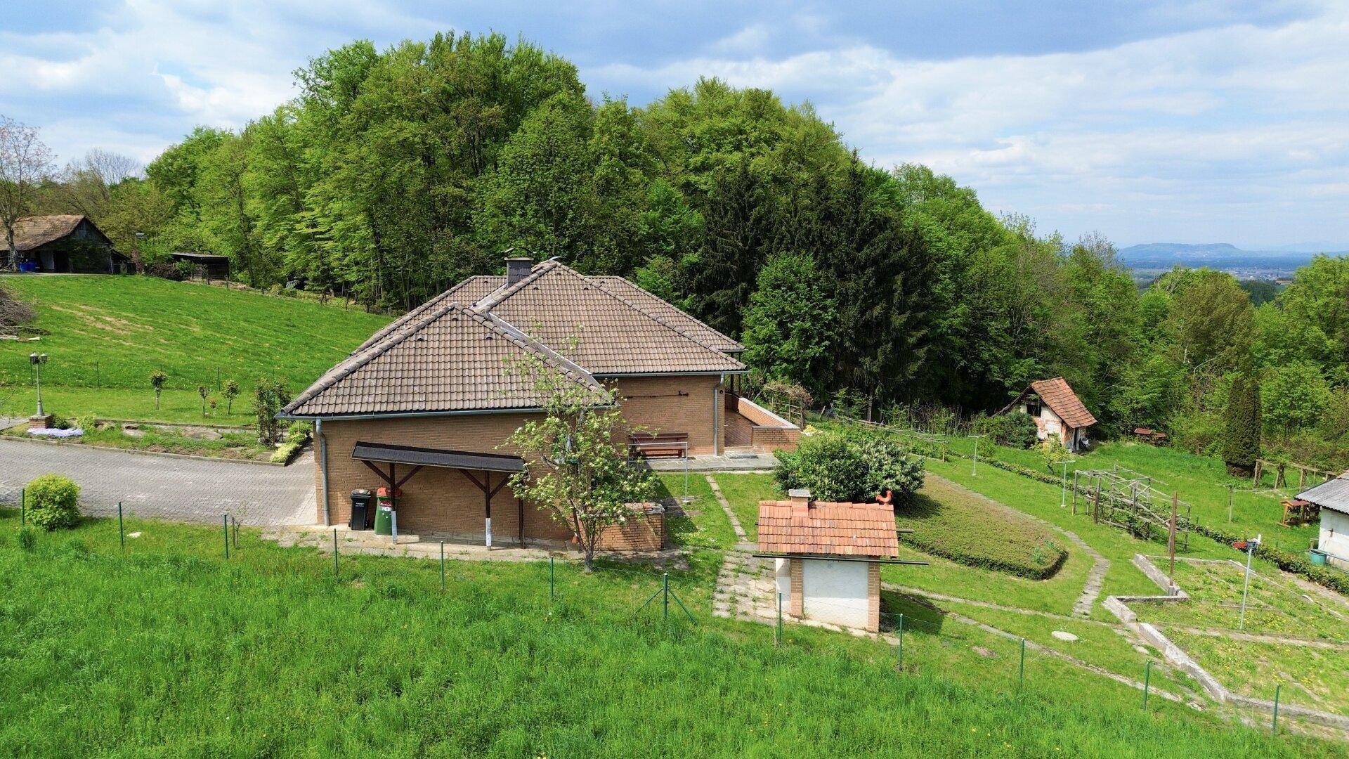 Seitenansicht des Hauses mit Gartenbereich, umgeben von dichtem Wald und grüner Natur.