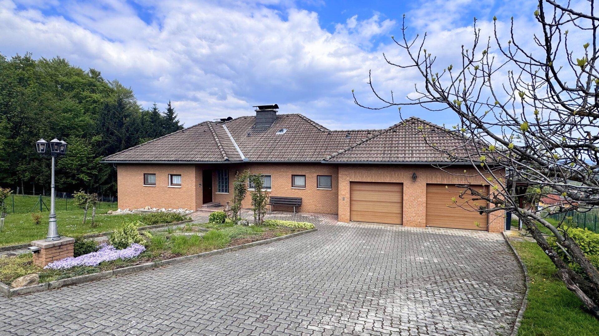 Frontansicht des Einfamilienhauses mit gepflasterter Auffahrt und Vorgarten unter blauem Himmel.