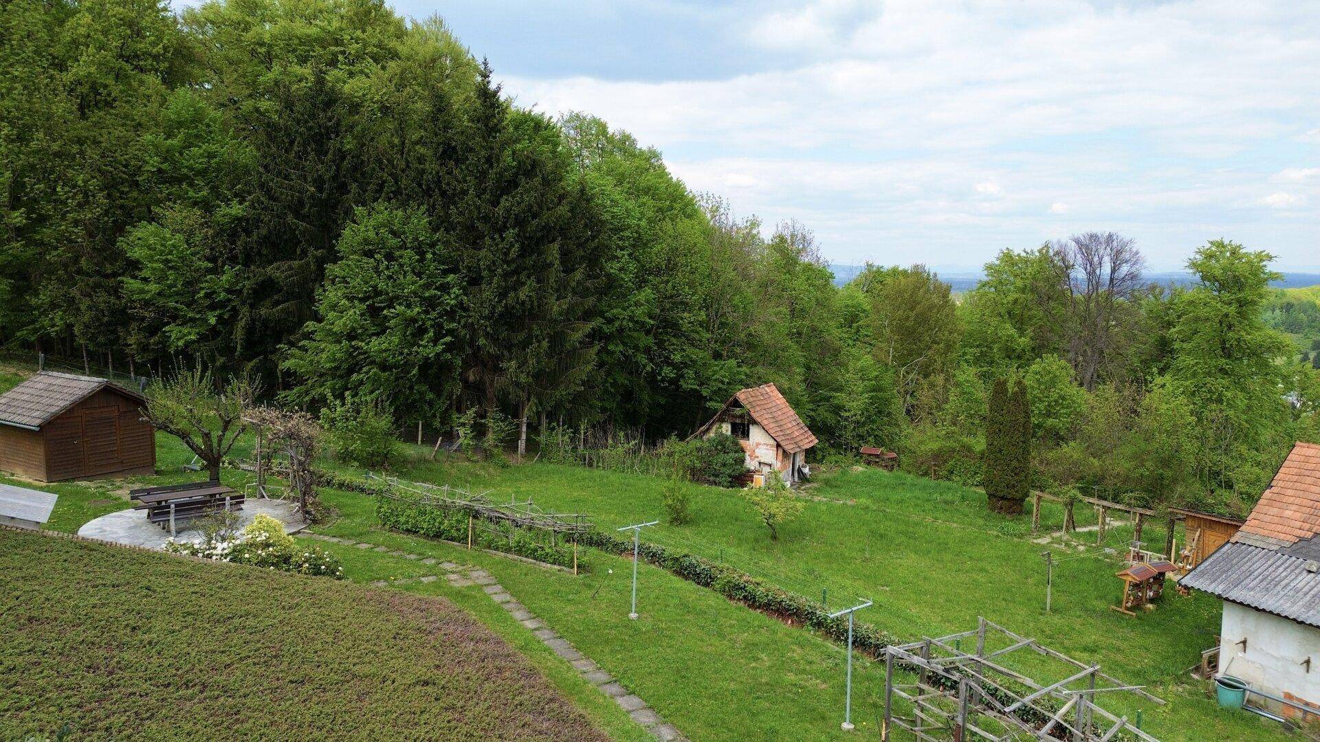 Weitläufiger Gartenbereich mit kleinen Nebengebäuden, umgeben von üppigem Grün und Wald.