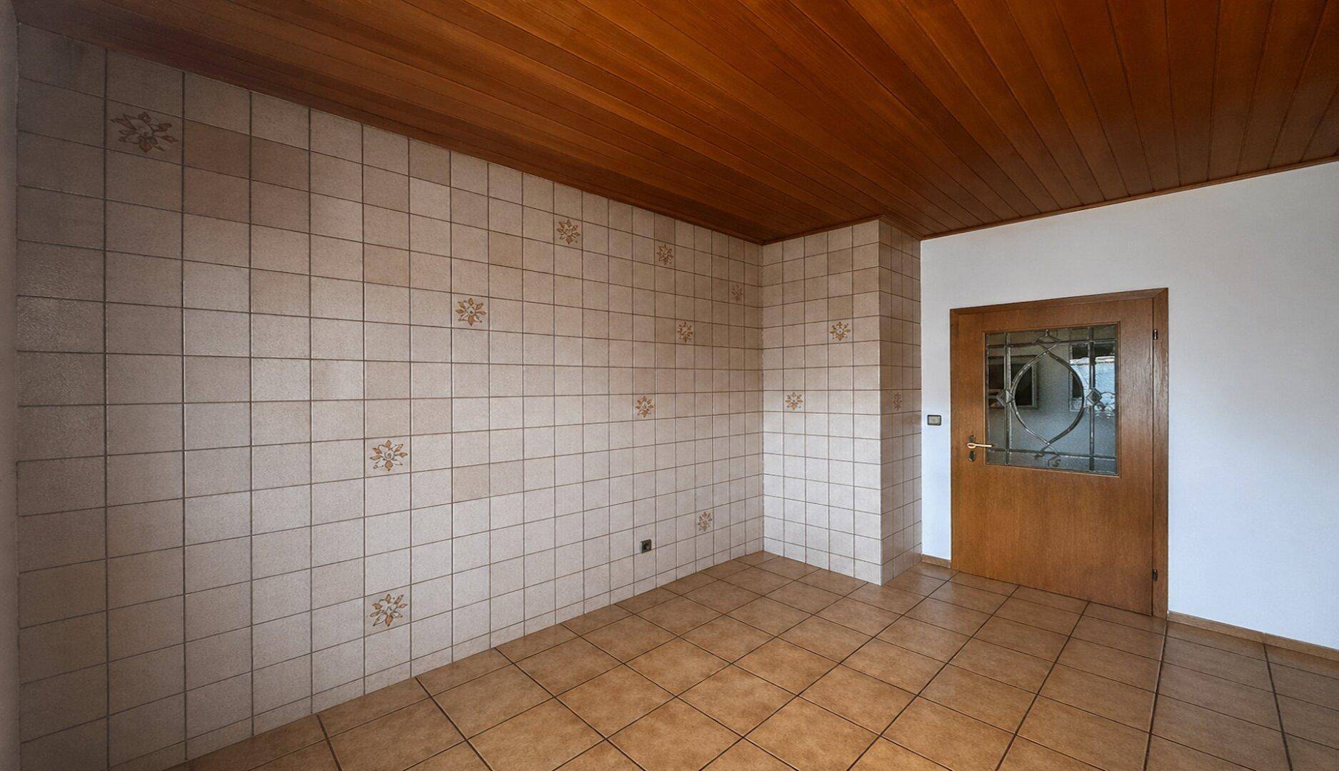 Raum mit dekorativ gefliesten Wänden, Holzdecke und einer Holztür, bereit für eine Kücheneinrichtung.