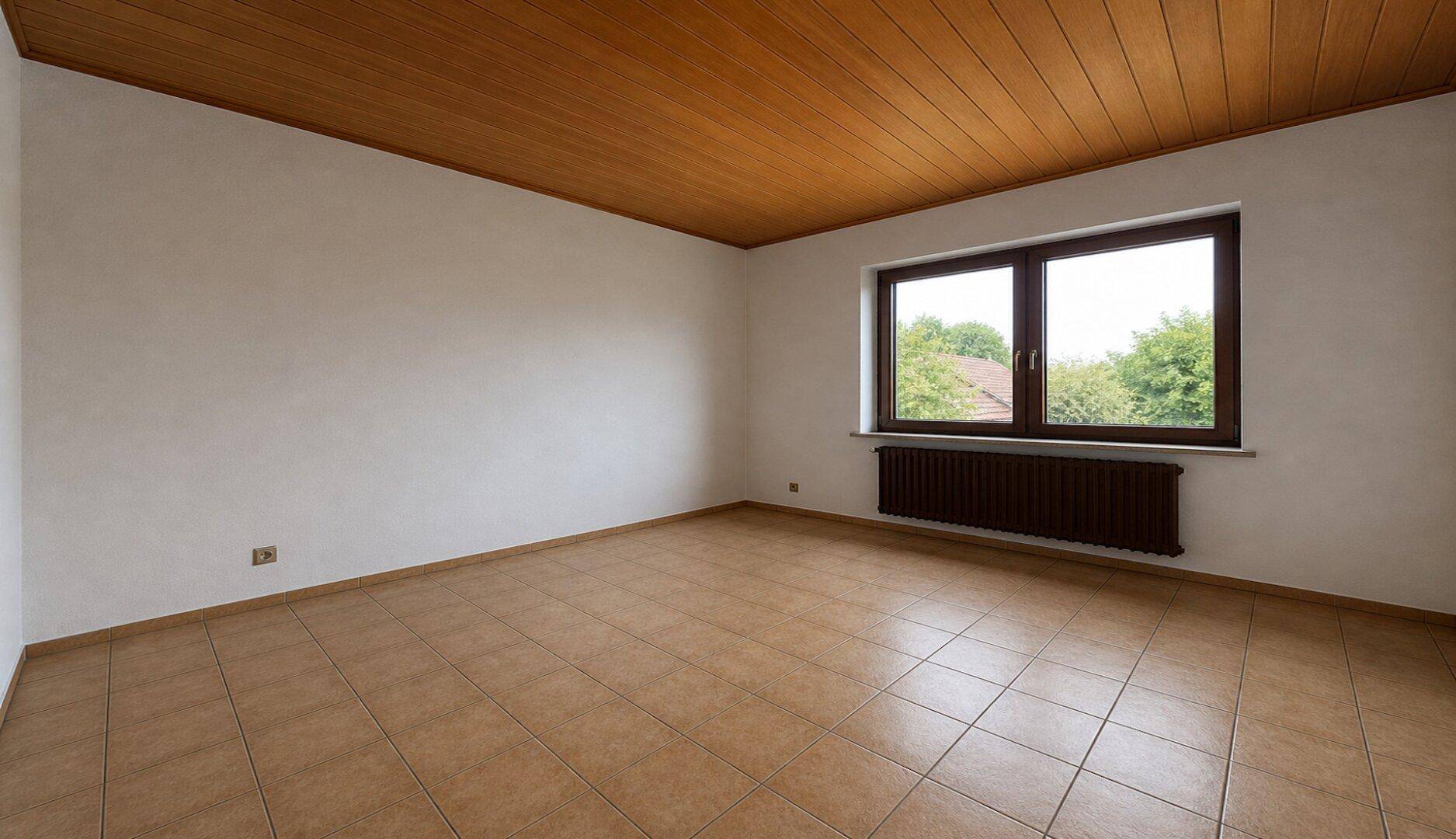 Leeres Schlafzimmer mit Fliesenboden, Holzdecke und einem großen Fenster mit Blick ins Grüne.