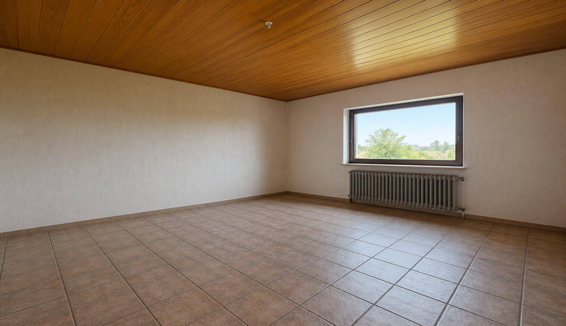 Heller, leerer Raum mit Fliesenboden, Holzdecke und einem Fenster mit weitem Ausblick.