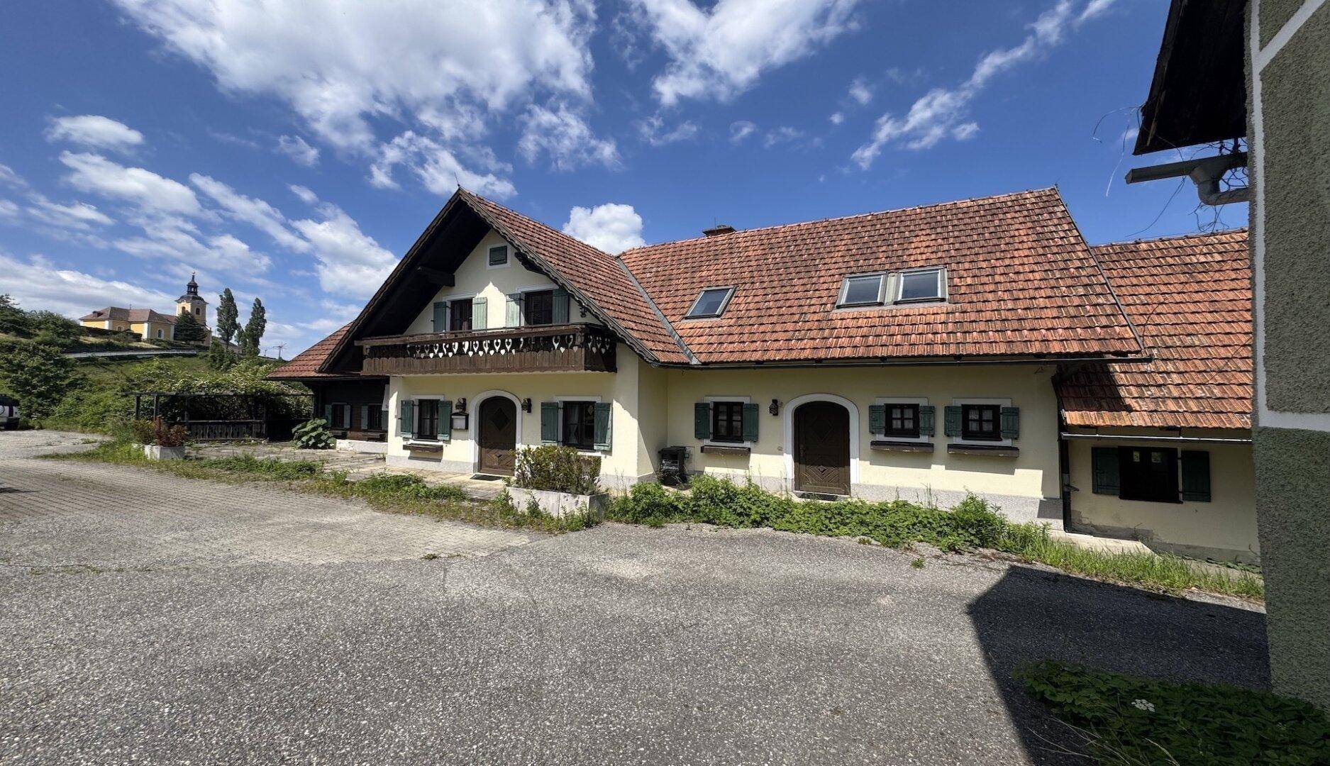 Traditionelles Haus mit Satteldach, Balkon und grünen Fensterläden in ländlicher Umgebung.