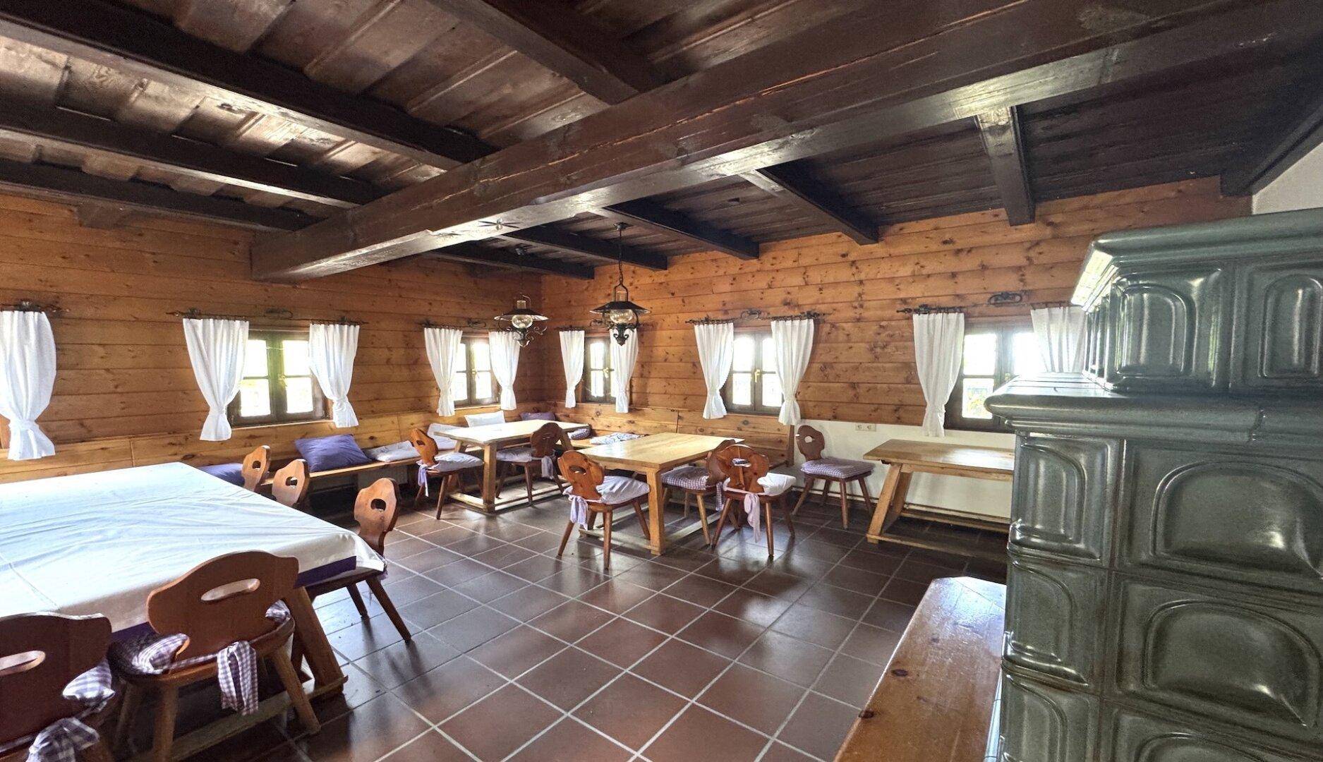 Traditionelle Stube mit Holzwänden, Holzbalkendecke und einem rustikalen Kachelofen.