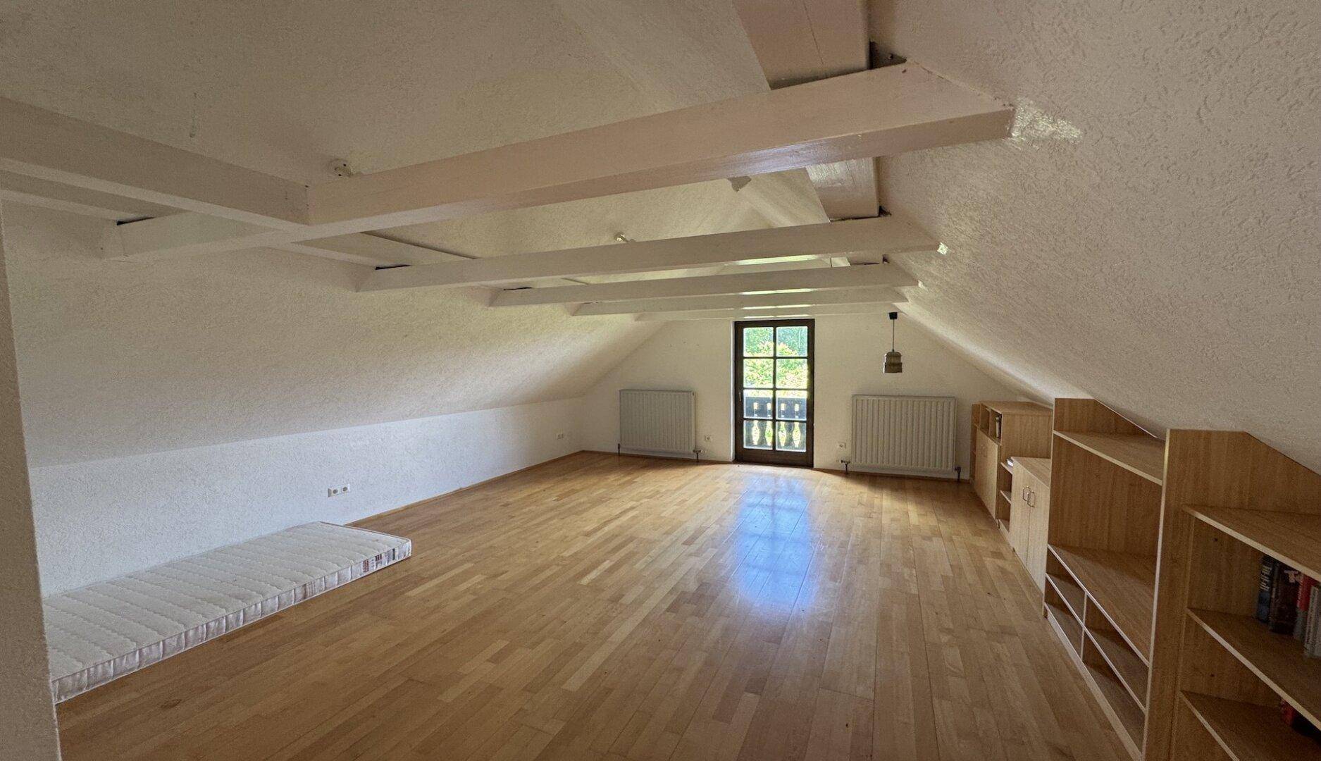 Geräumiger Dachbodenraum mit sichtbaren Holzbalken, Dachschräge und Balkonzugang.