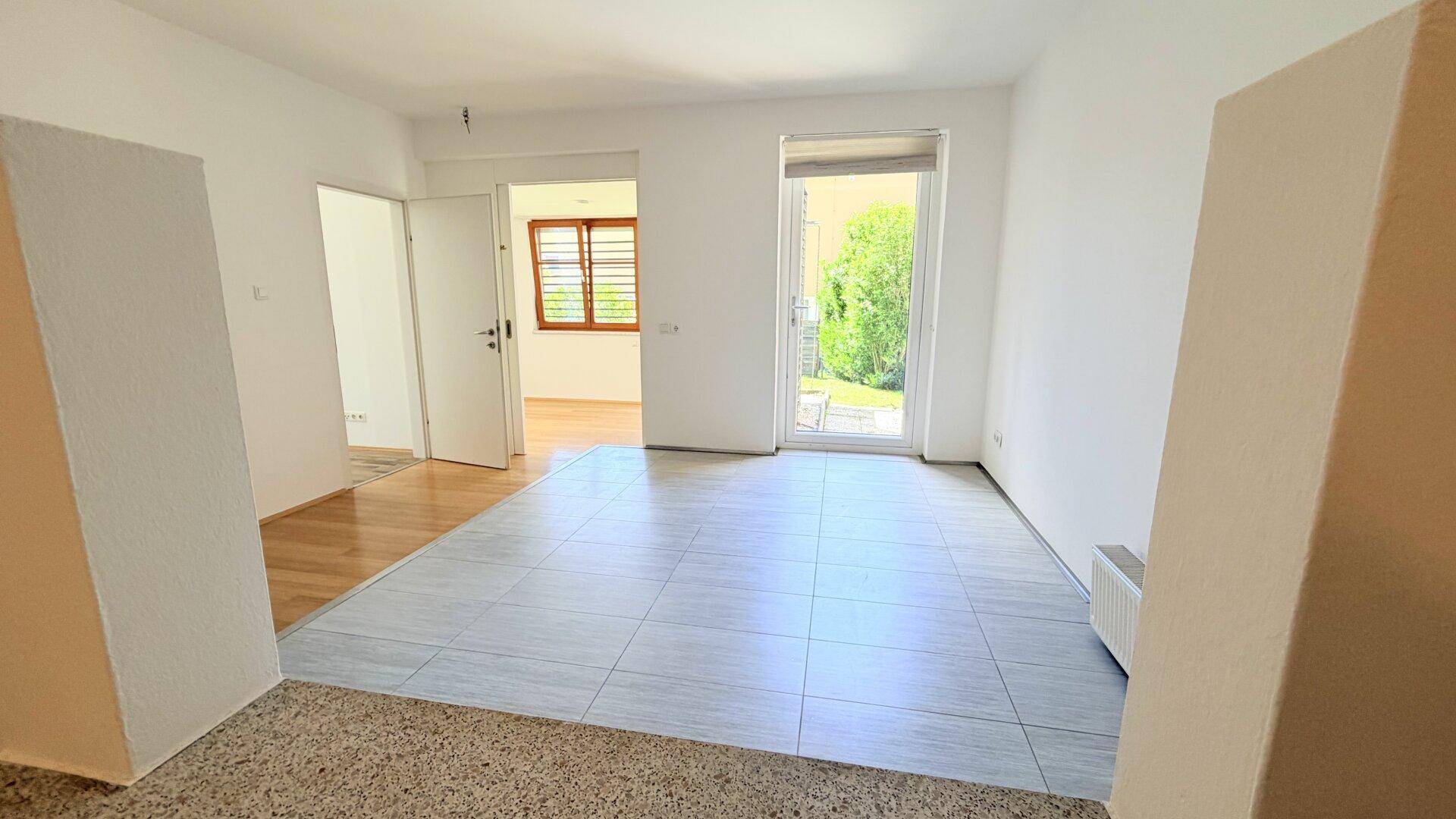 Heller, leerer Raum mit Fliesenboden und Zugang zum Garten durch eine große Terrassentür.