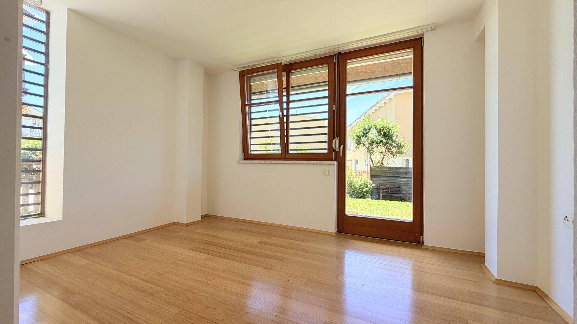 Helles Schlafzimmer mit Holzfußboden und großem Fenster mit Zugang zum Außenbereich.