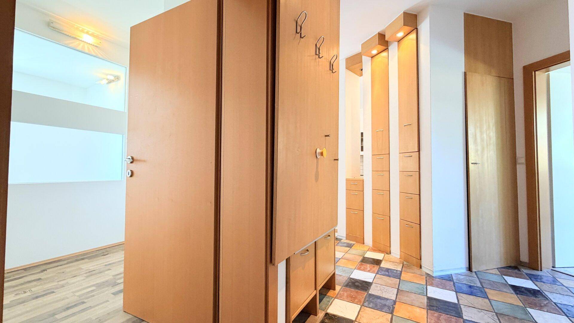 Eingangsbereich mit bunten Fliesen, integrierten Garderobenschränken und Holzvertäfelung.
