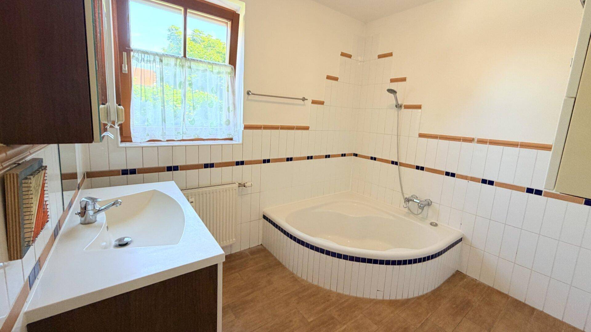 Badezimmer mit Eckbadewanne, Einzelwaschbecken und Fenster, dekoriert mit blauen Akzenten.