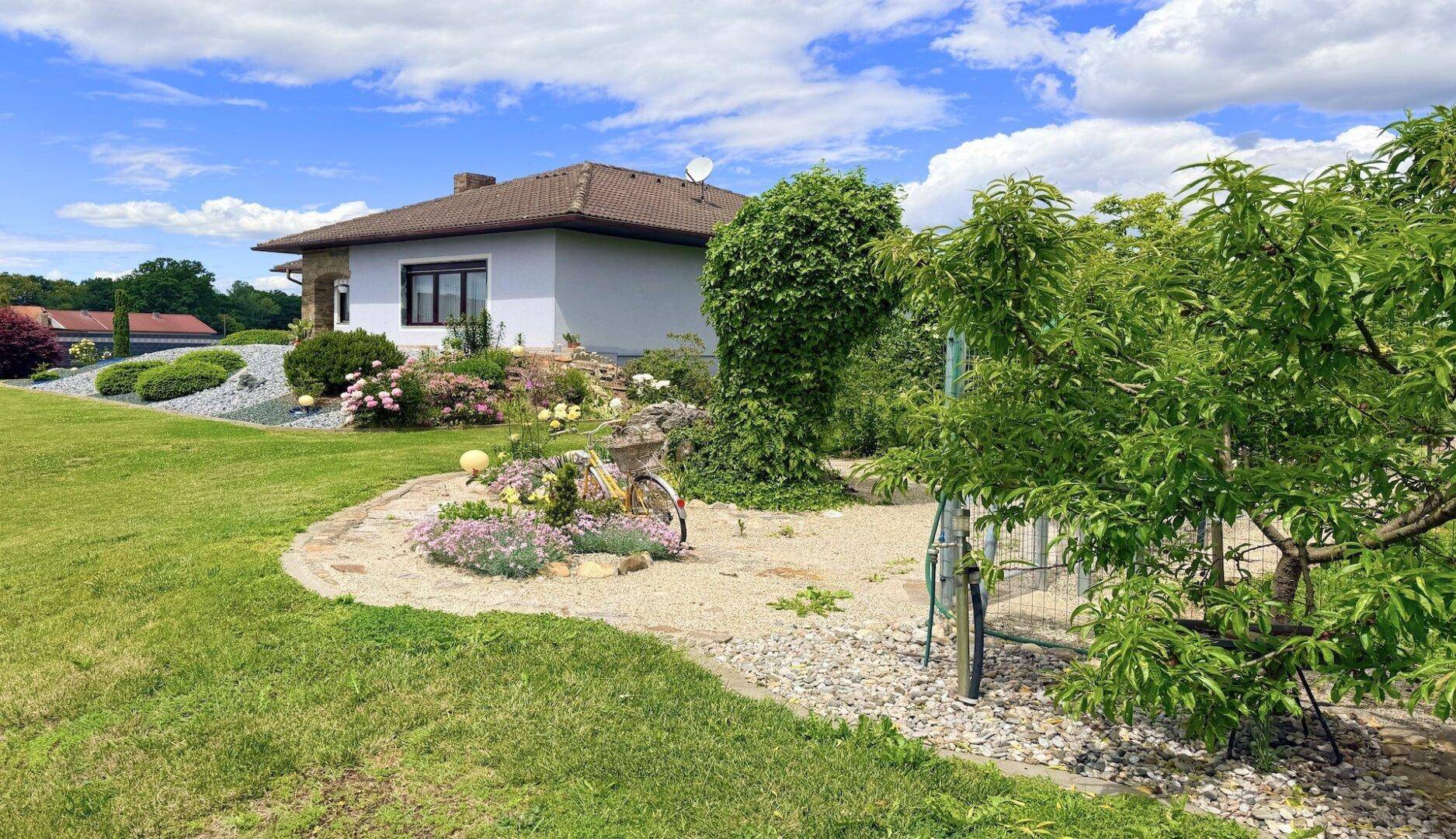 Gepflegter Gartenbereich mit Blumenbeeten und Obstbäumen vor dem Haus unter blauem Himmel.