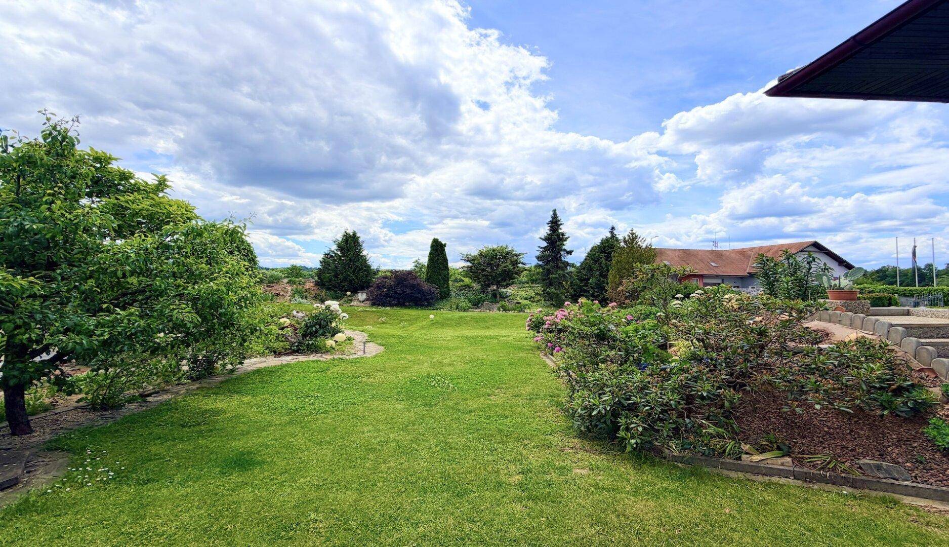 Großer, gepflegter Garten mit Rasenflächen und vielfältiger Bepflanzung unter weitem Himmel.