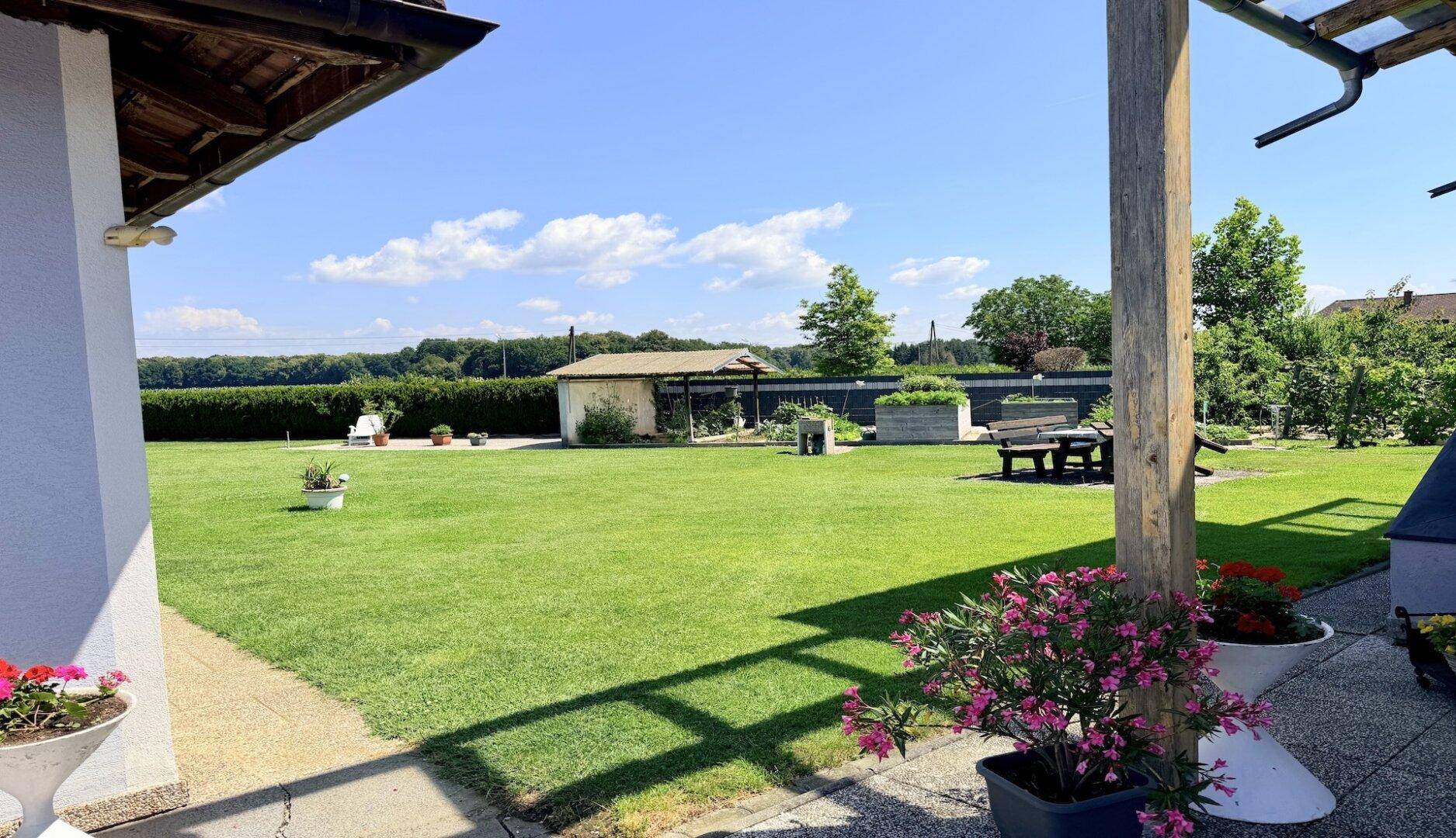 Weitläufiger Garten mit Rasen, Sitzgelegenheiten und Blick auf die grüne Umgebung.