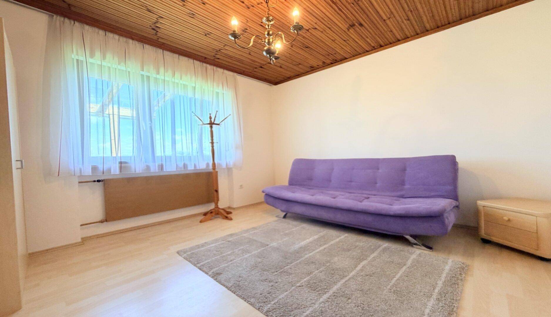 Helles Zimmer mit Holzdecke, Parkettboden und einem lila Sofa.