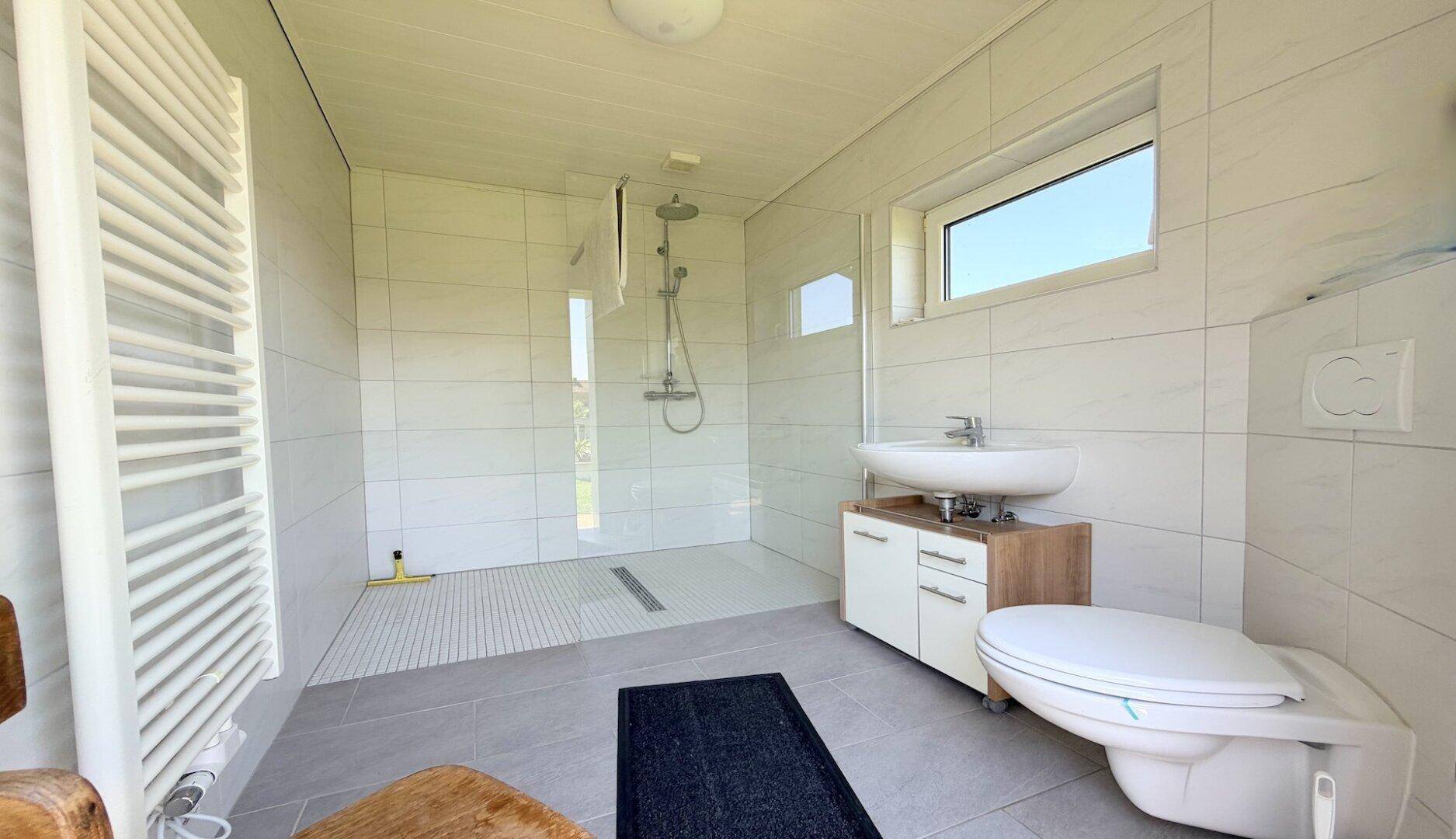 Modernes Badezimmer mit ebenerdiger Dusche, Handtuchheizkörper und Fenster.