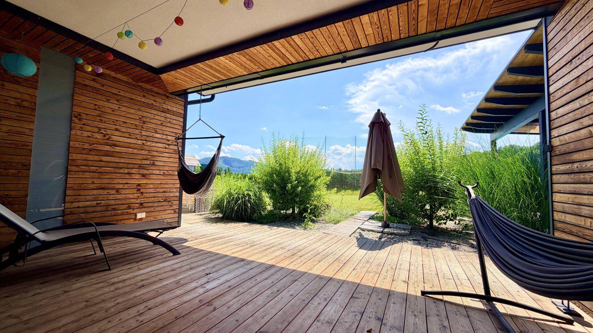 Heller, offener Terrassenbereich mit Holzwänden, Hängematten und Zugang zum Garten.