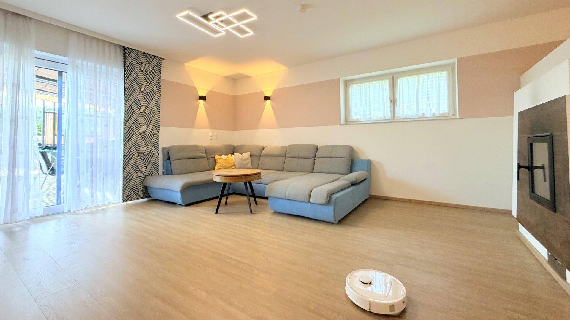 Modernes Wohnzimmer mit Ecksofa, hellem Laminatboden und Zugang zur Terrasse.