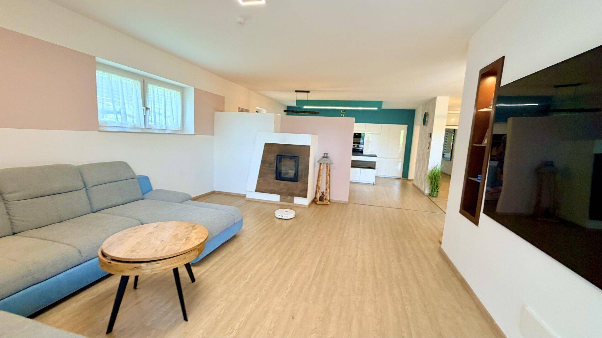 Offener Wohnbereich mit Sofa, Kamin und Blick auf die moderne Küche.