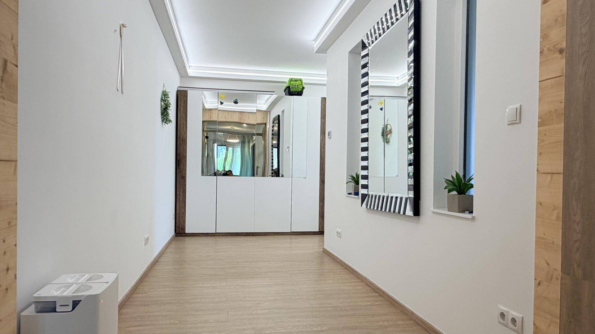 Heller Flur mit Laminatboden, Spiegelschrank und indirekter Beleuchtung.