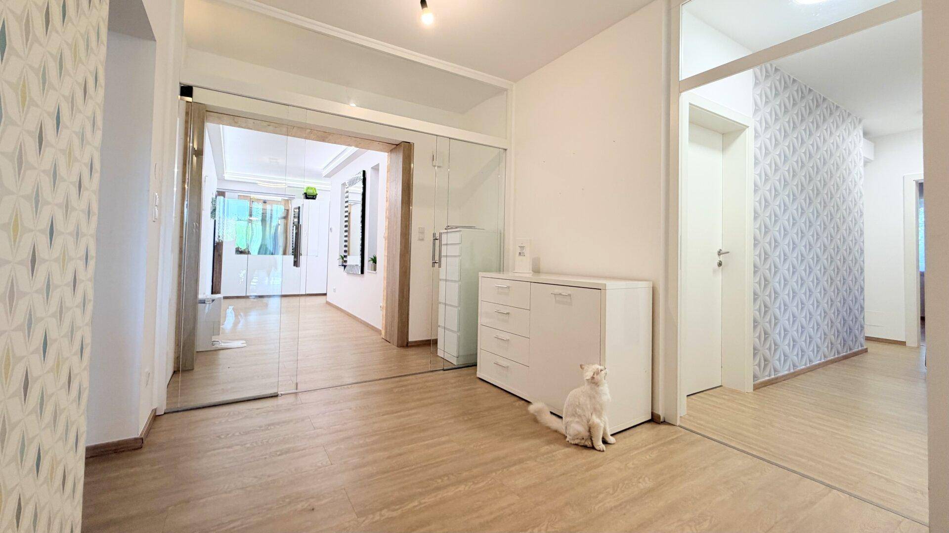 Geräumiger Flur mit Laminatboden, weißer Kommode und dekorativer Tapete.