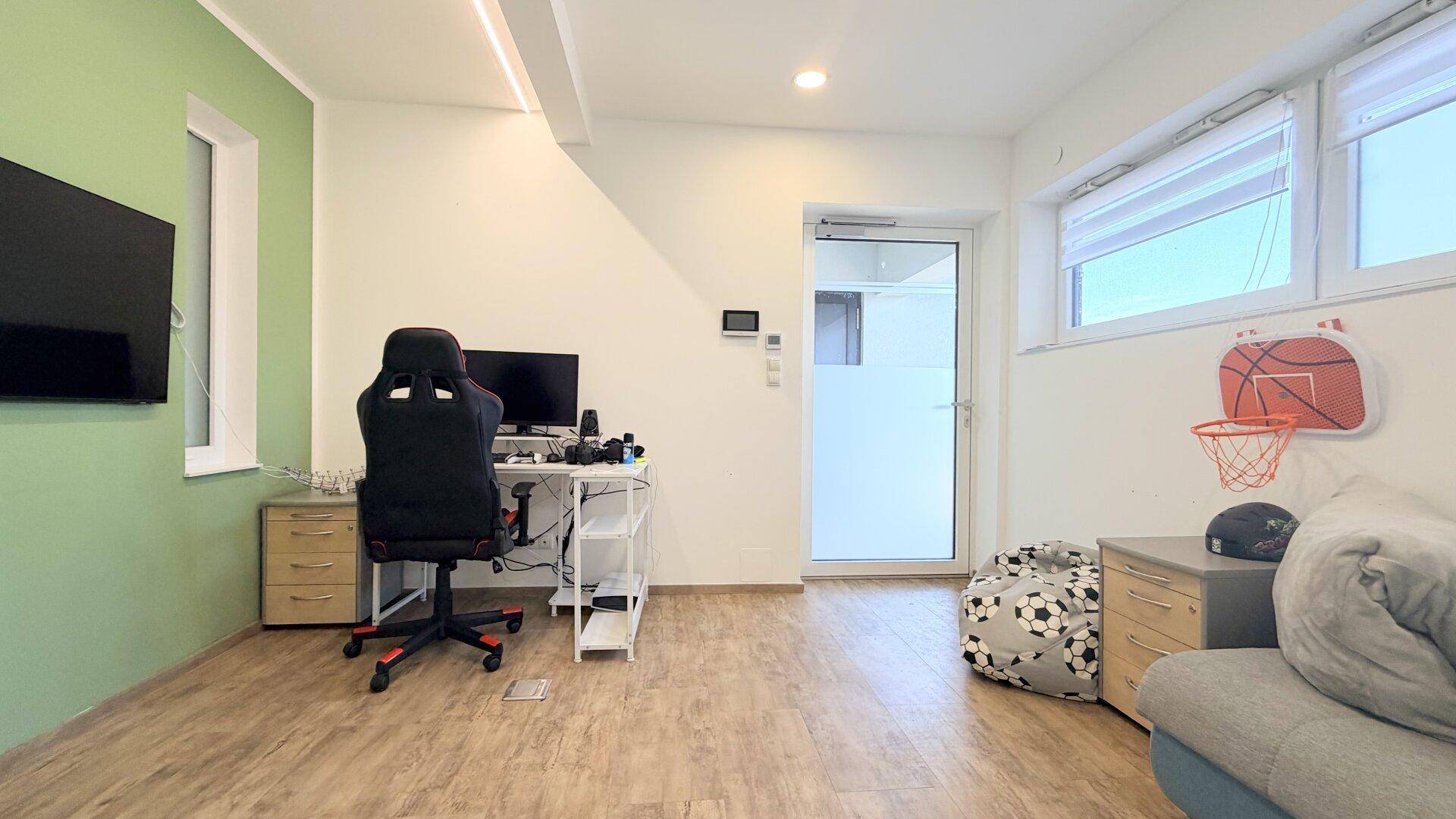 Helles Arbeitszimmer mit Schreibtisch, Gaming-Stuhl und Fenster.