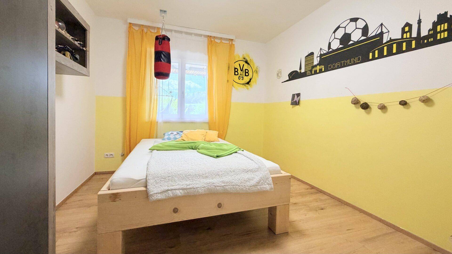 Kinderzimmer mit Einzelbett, gelben Wänden und dekorativer Wandgestaltung.