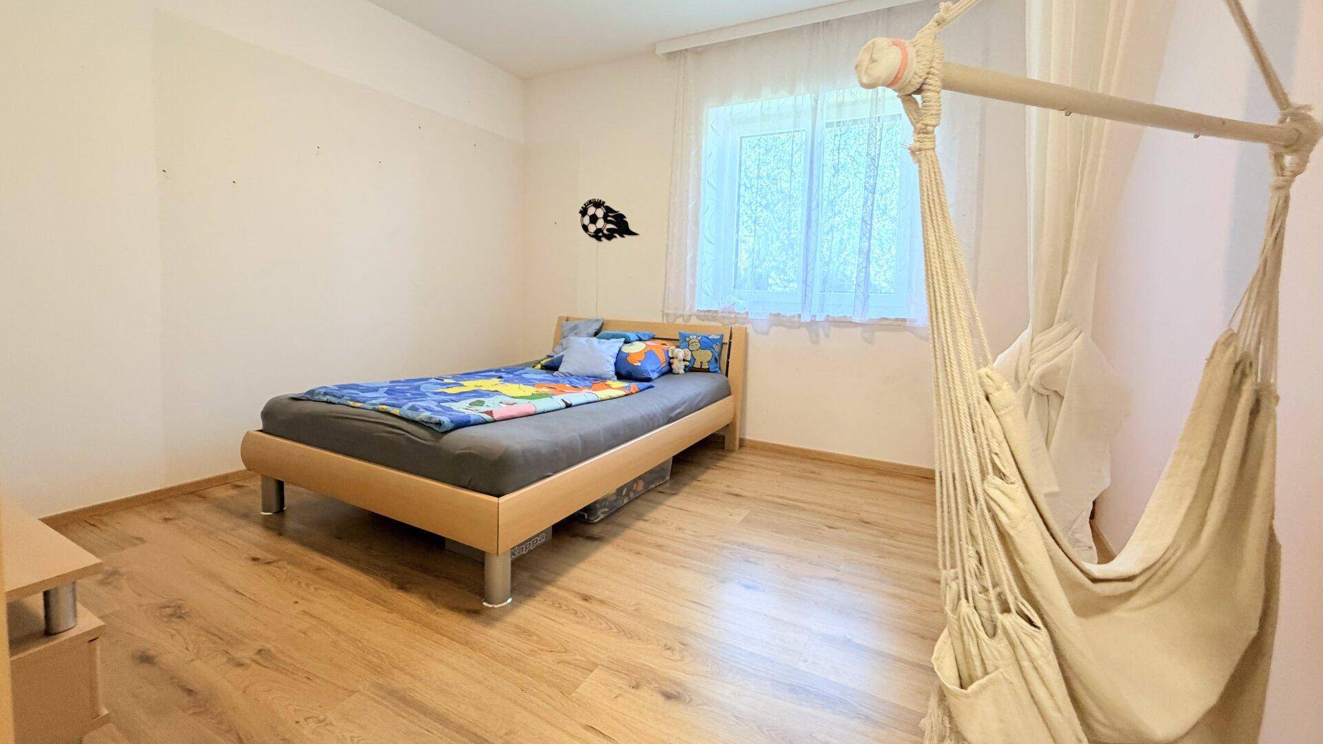 Helles Kinderzimmer mit Einzelbett, Hängesessel und großem Fenster.