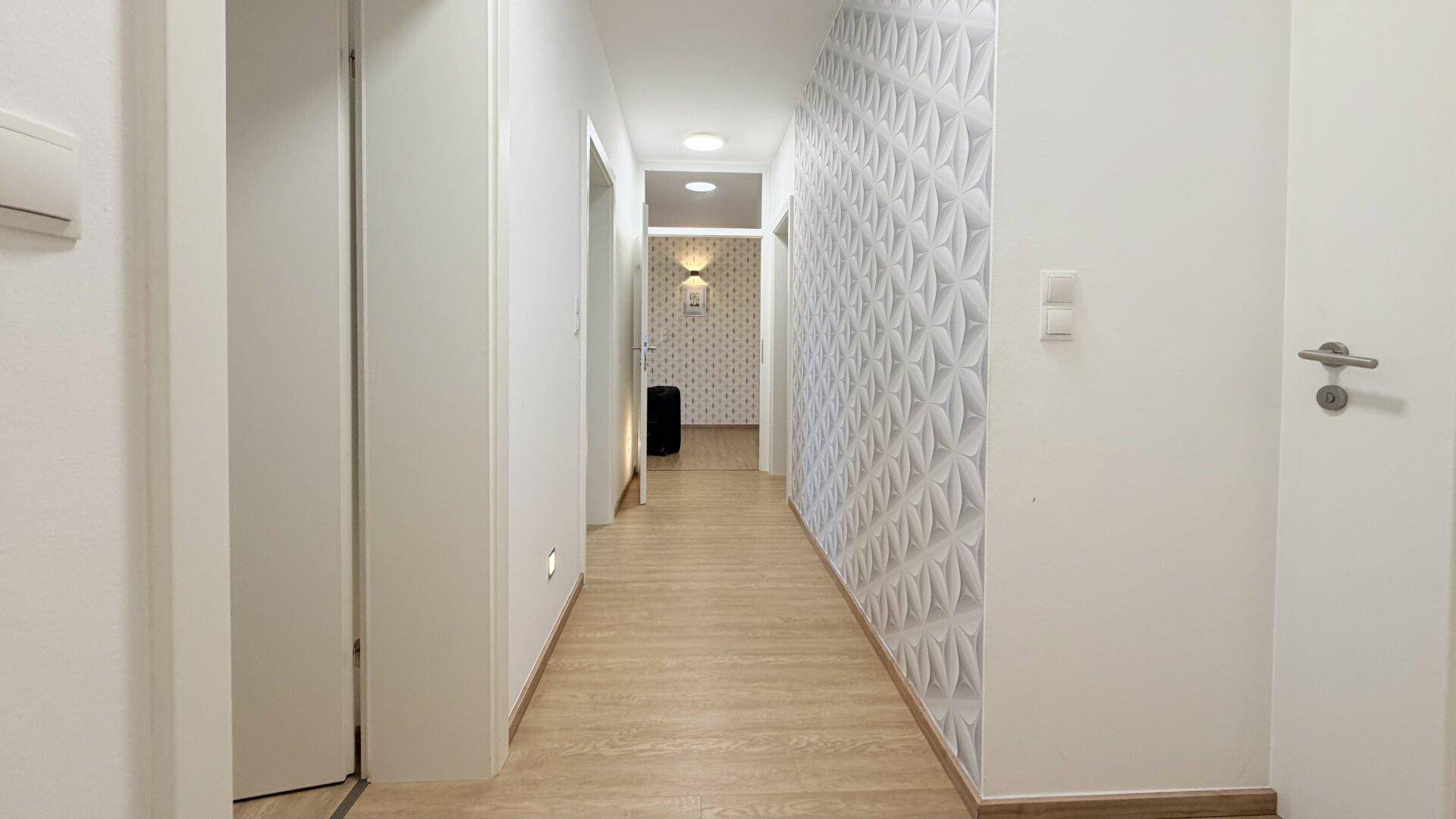 Langer Flur mit Laminatboden und moderner 3D-Tapete.