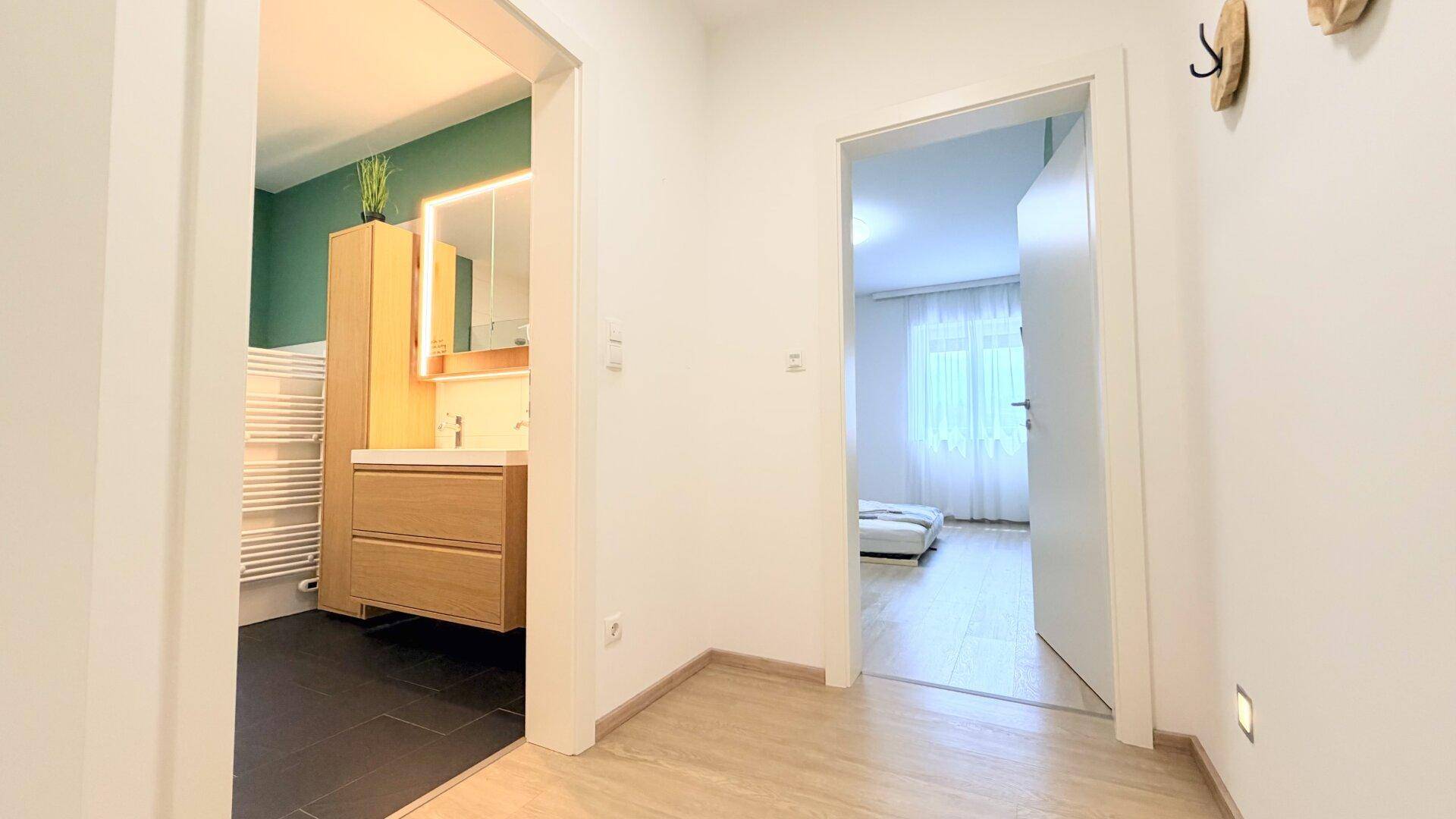 Heller Flur mit Holzboden, der zu einem modernen Badezimmer und Schlafzimmer führt.