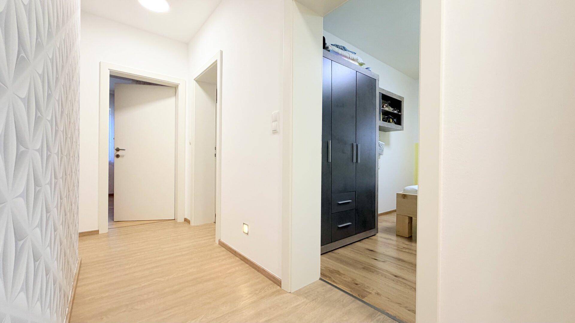Heller Flur mit strukturierten Wänden und Holzboden, der zu einem weiteren Raum führt.