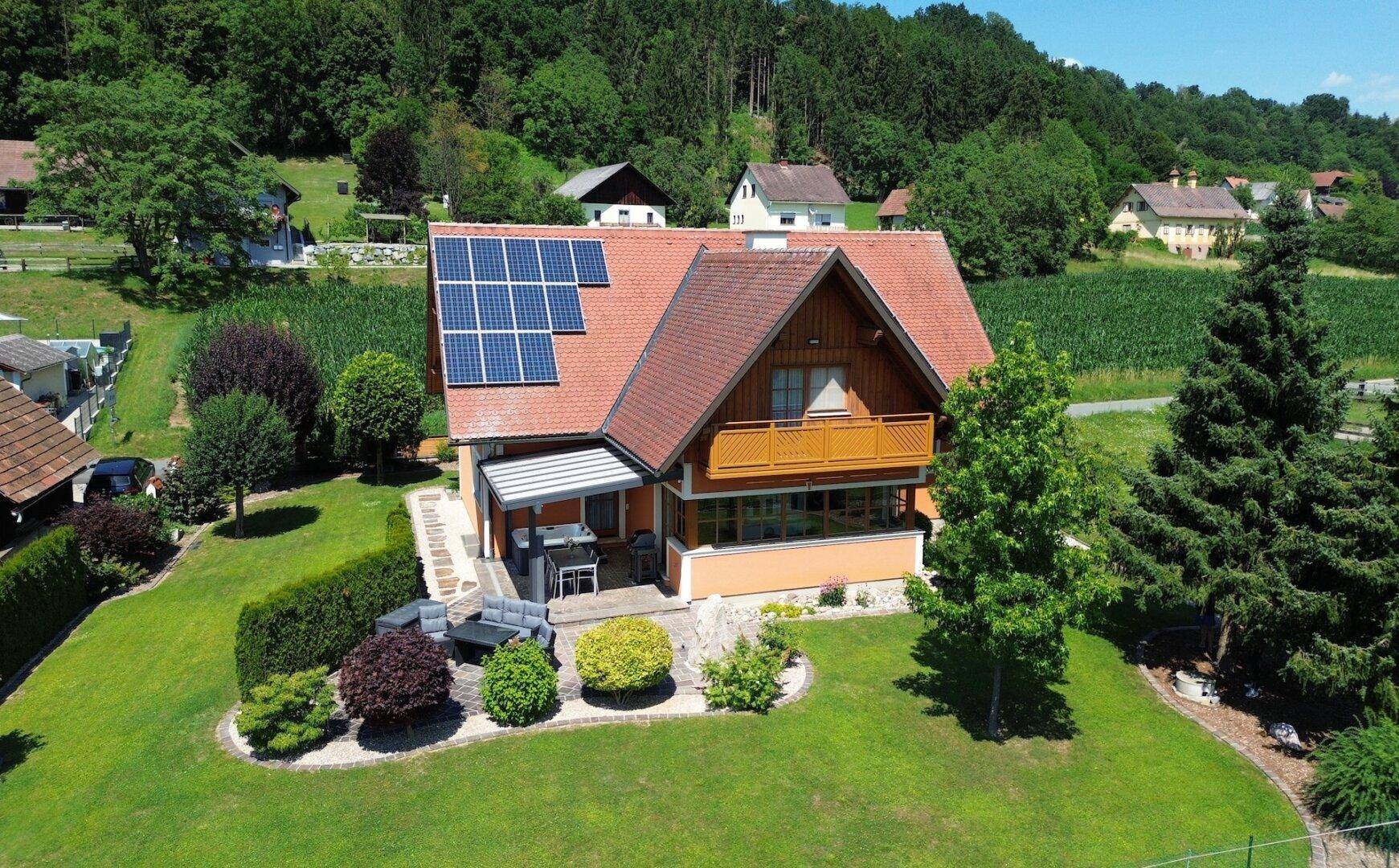 Weitläufiger Gartenbereich mit Einfamilienhaus, Photovoltaikanlage und Sitzgelegenheiten im Freien.