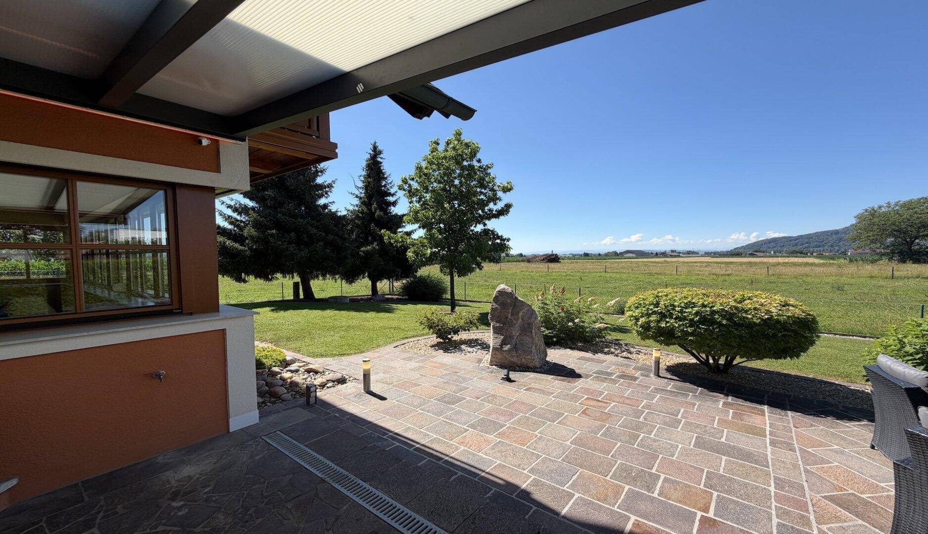 Überdachte Terrasse mit Steinplatten und weitem Blick über die umliegenden Felder.