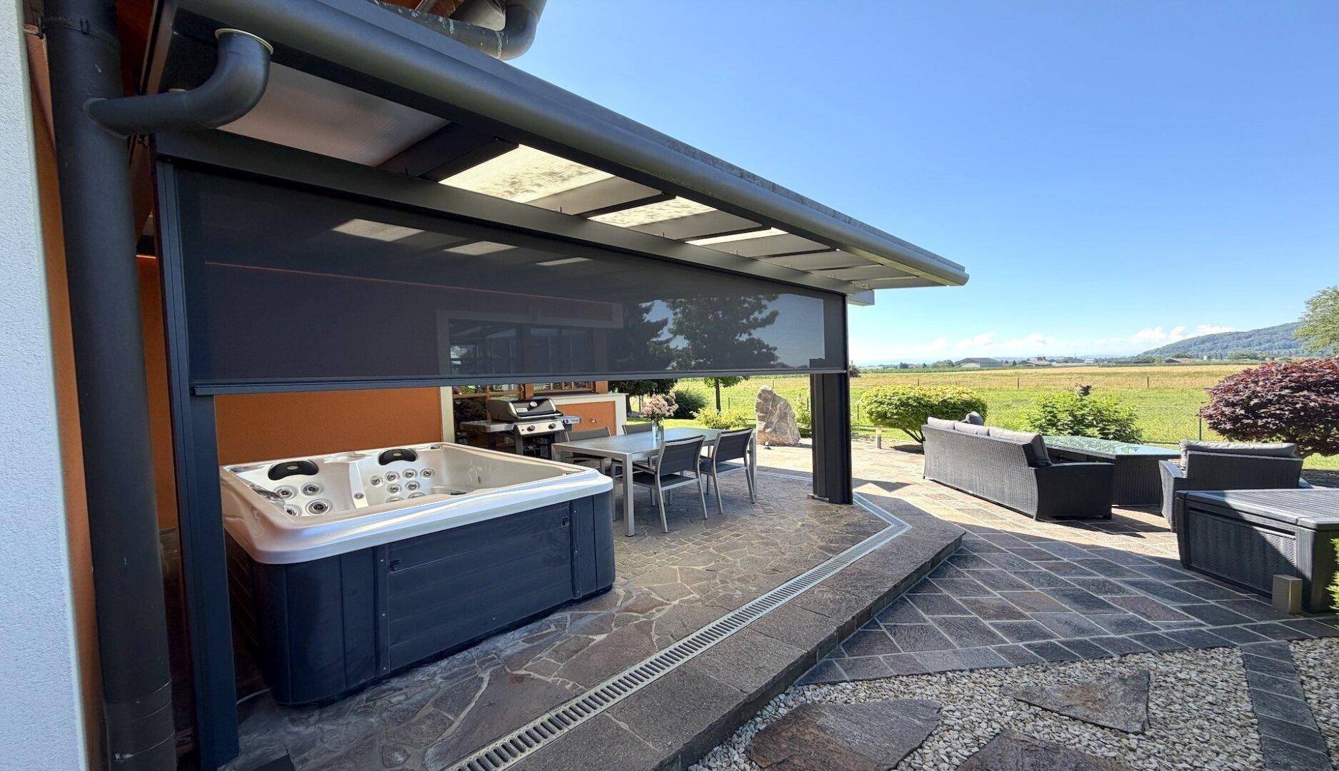Überdachte Terrasse mit Whirlpool, Grillbereich und weiteren Sitzgelegenheiten im Freien.