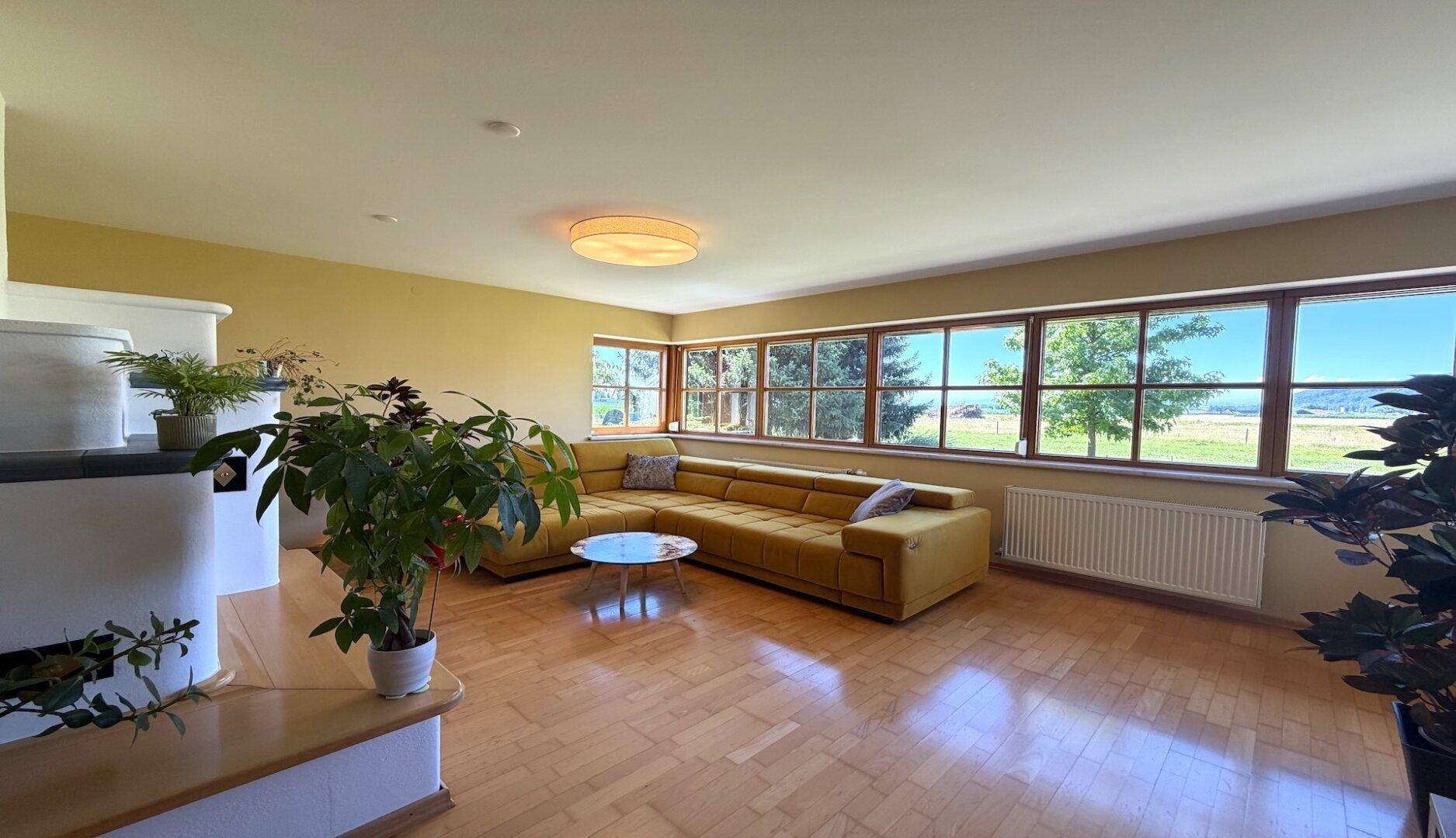 Lichtdurchflutetes Wohnzimmer mit Holzboden, gemütlichem Sofa und Panoramablick.